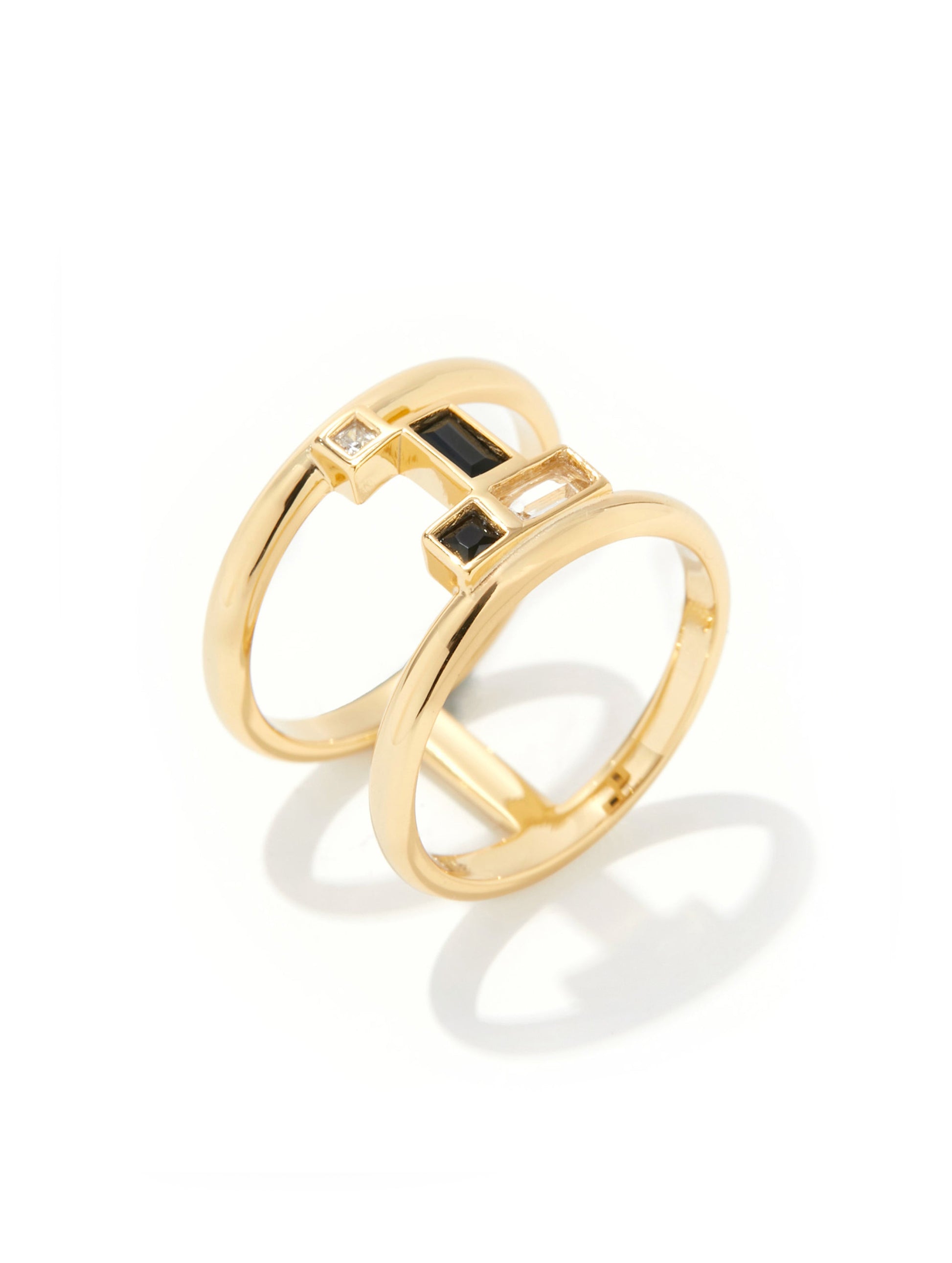A gold ring featuring a geometric design with a central square bezel-set black stone and small clear stones, photographed on a clean white background with a soft shadow.