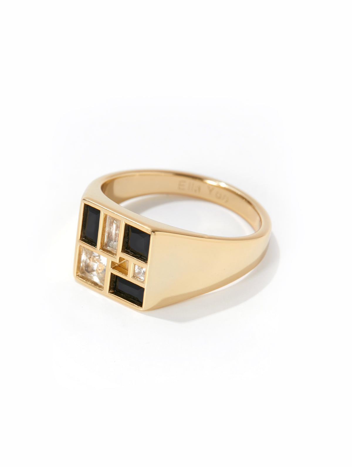 A gold signet ring featuring a geometric face with alternating black and clear rectangular stones, set against a plain white background.