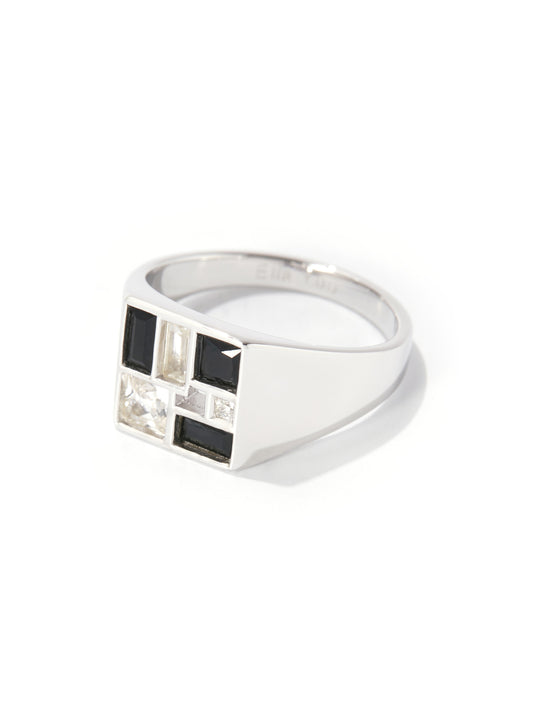 A silver signet ring featuring a geometric face with alternating black and clear rectangular stones, set against a plain white background.