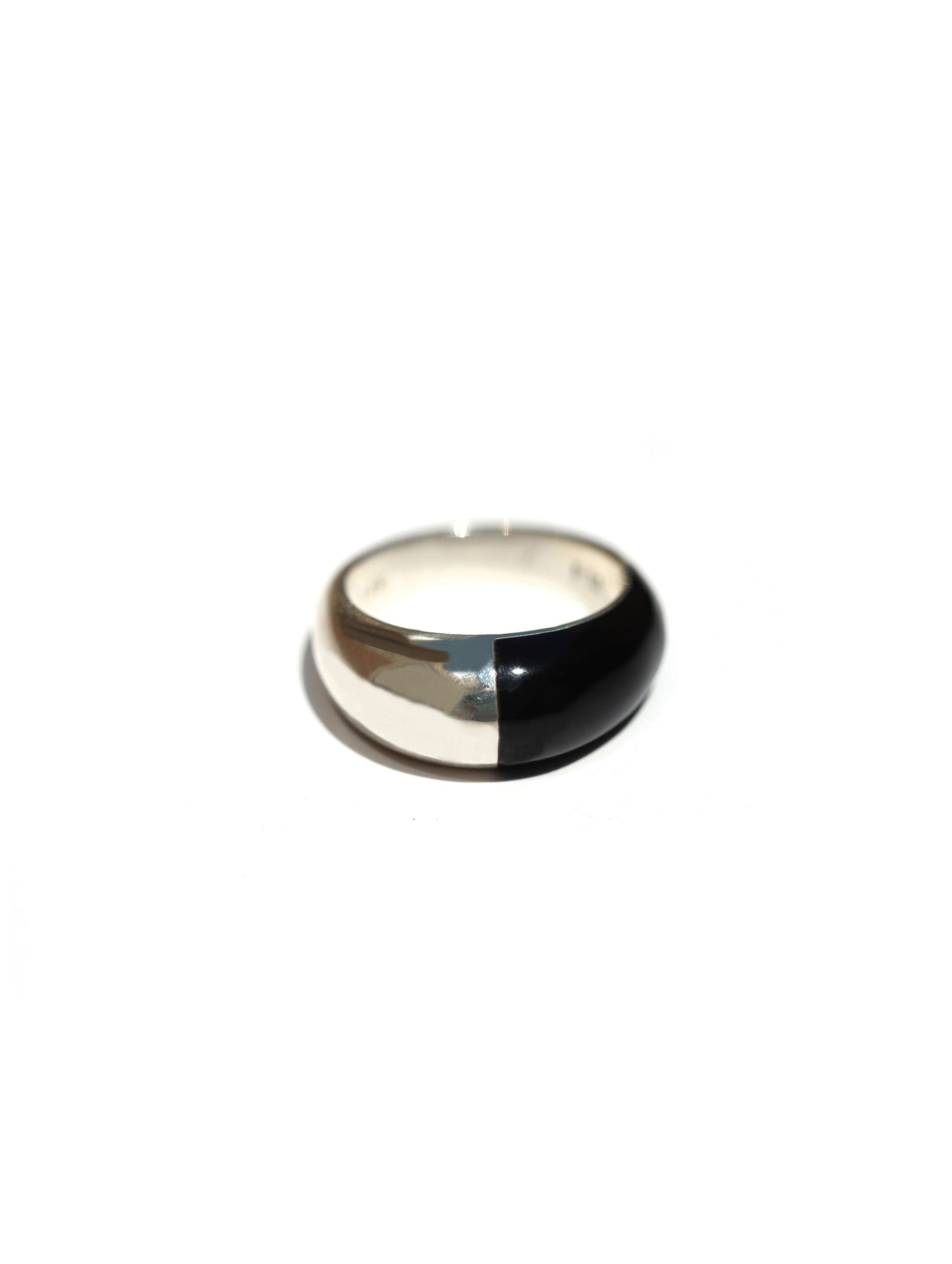 A minimalist dome ring with a split design, featuring a polished silver half and a glossy black half, set against a plain white background.