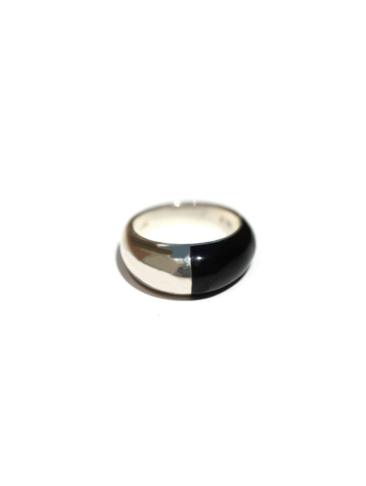 A minimalist dome ring with a split design, featuring a polished silver half and a glossy black half, set against a plain white background.