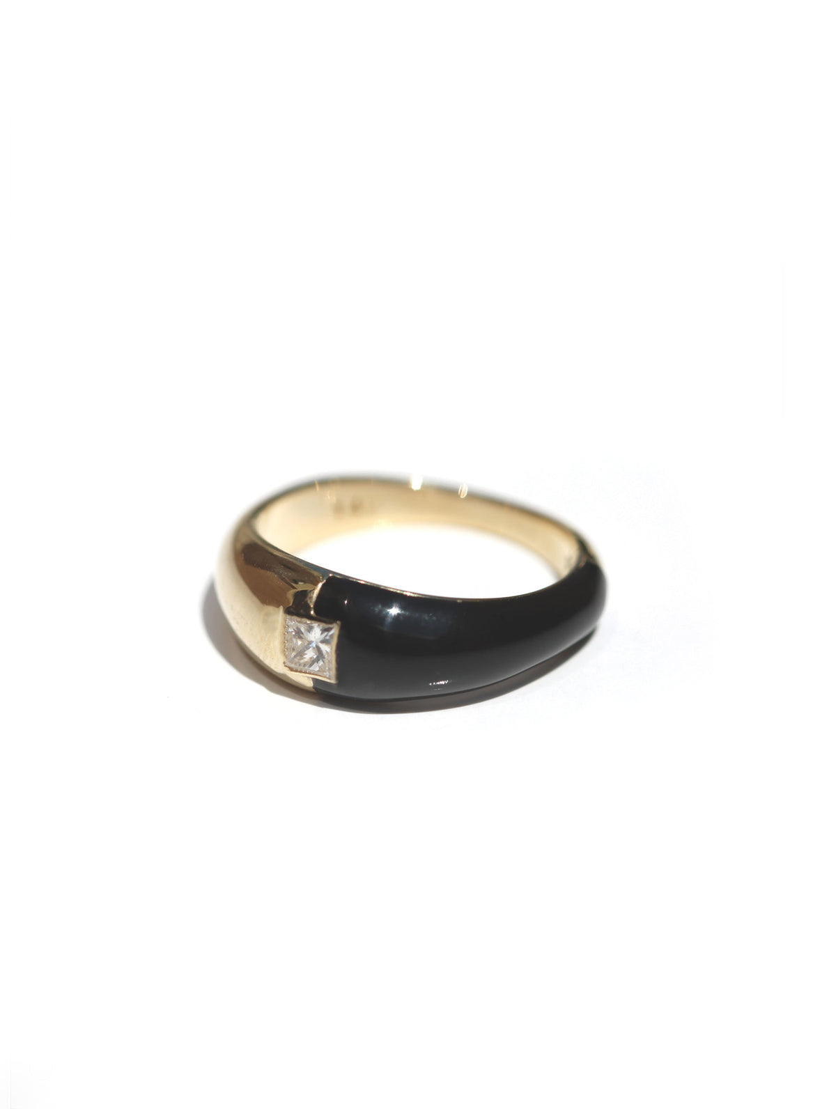 A gold ring with a glossy black enamel inlay and a small square clear gemstone, photographed on a plain white background.