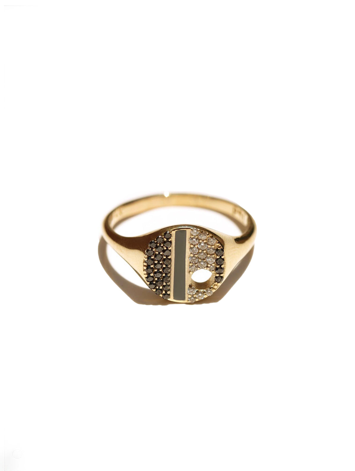 A gold signet ring with a split face, one half paved with small clear stones and the other half featuring a central vertical bar of dark oxidized metal and a small circular cutout, shown on a white background with a soft shadow.